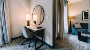 A hotel room with a desk, chair, lamp, mirror, and a blue sofa.