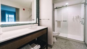 A bathroom with a large mirror, two sinks, a shower, and a toilet.