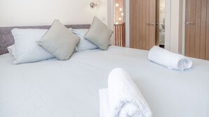 Un letto rifatto con cuscini e un asciugamano arrotolato, ante di un armadio in legno e un lampadario fissato alla parete.