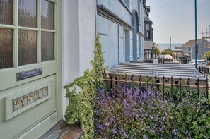 Ein charmantes Reihenhaus mit einer grünen Tür, auf der "MYRTLE" steht, einem Holzzaun und einem Garten mit violetten Blumen.