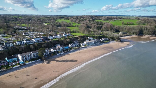 Vista aerea di una località costiera con spiaggia, case e campi verdi.