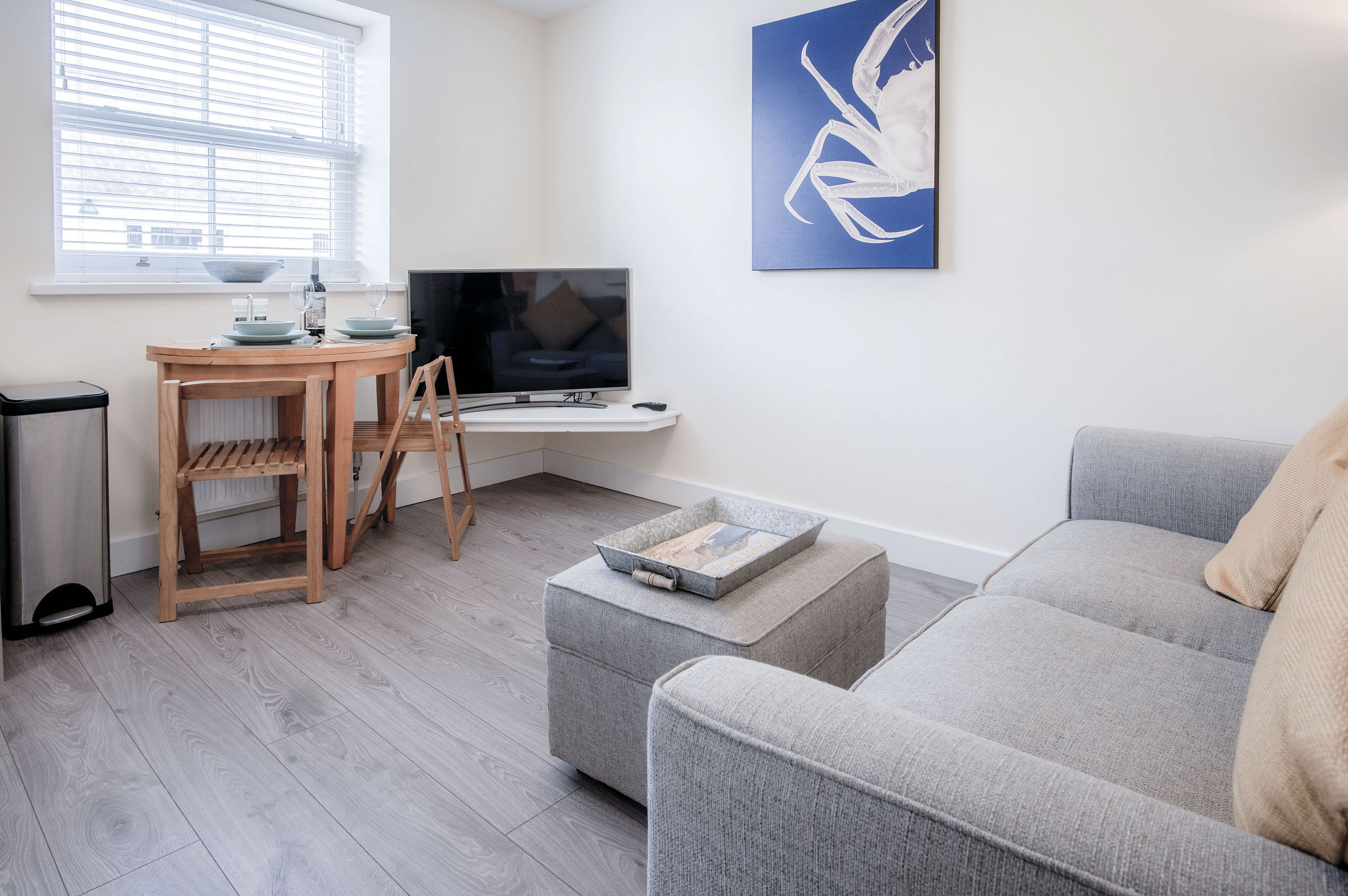Ein modernes Wohnzimmer mit einem grauen Sofa, einem Holzesstisch mit Stühlen, einem Fernseher und einem Gemälde an der Wand.