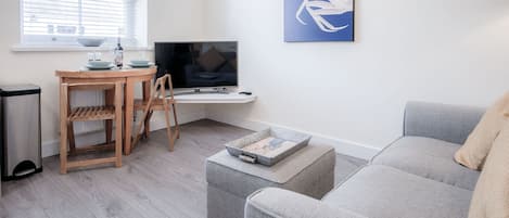 Una sala de estar moderna con un sofá gris, una mesa de comedor de madera con sillas, un televisor y un cuadro en la pared.
