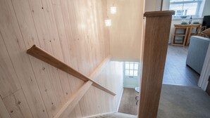 Una scala in legno con un pianerottolo rivestito di tappeto, che conduce a una stanza con un tavolo da pranzo e un divano grigio.