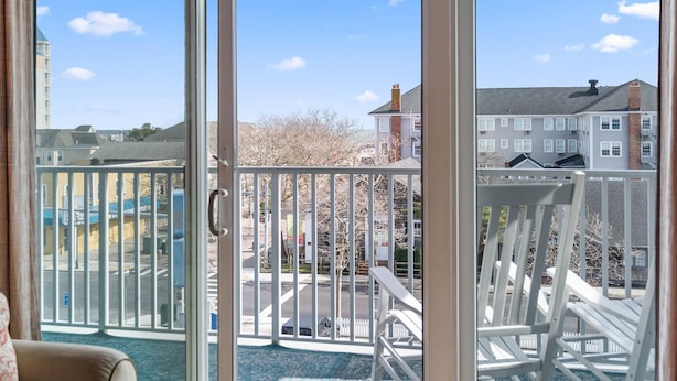 A balcony with a view of a residential area, a white chair, and a glass door.