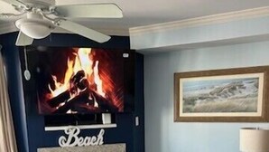 A living room with a fireplace, a television mounted above it, a ceiling fan, and a framed picture on the wall.