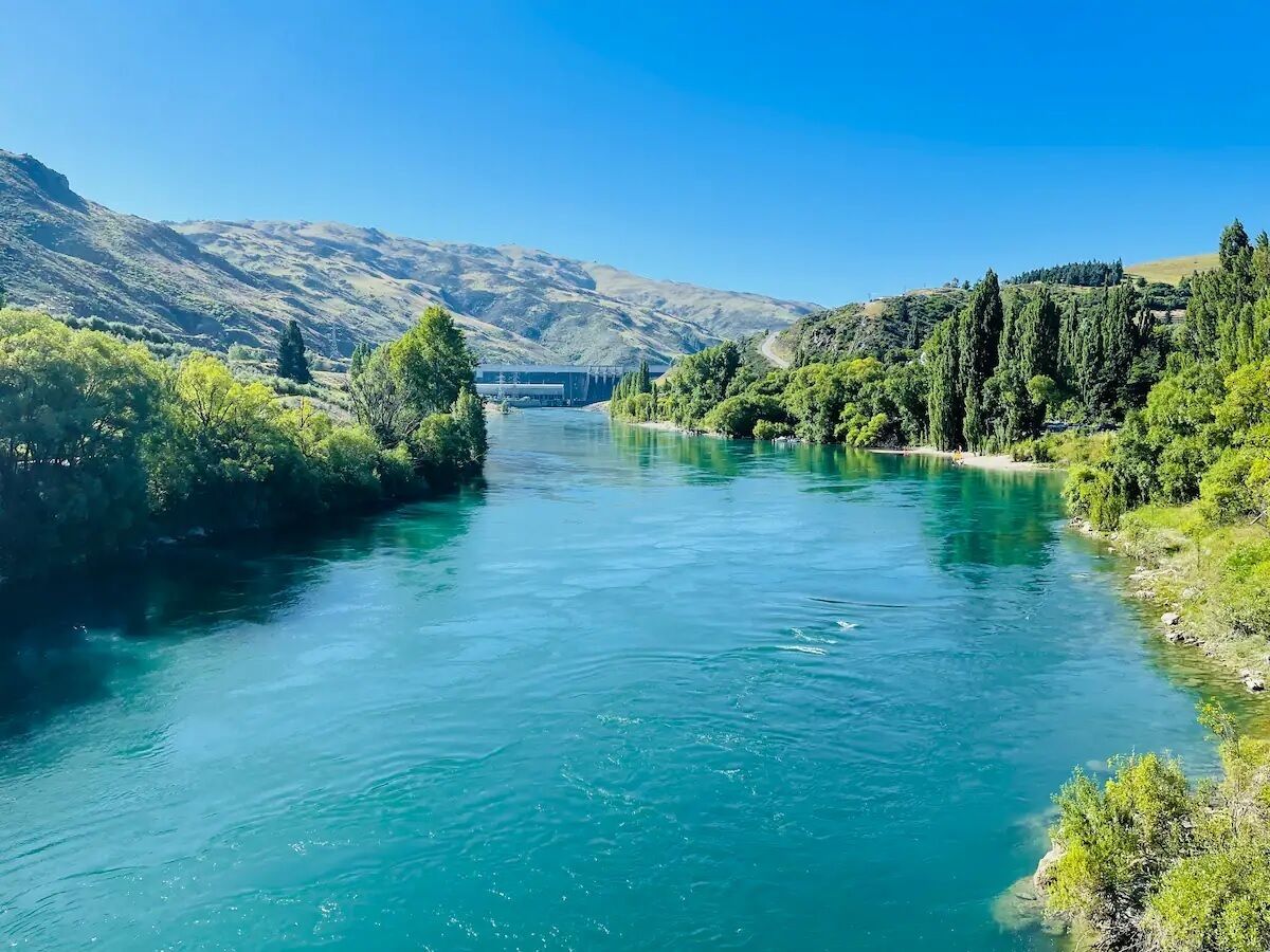 Un río con un puente a lo lejos, rodeado de colinas verdes y árboles.