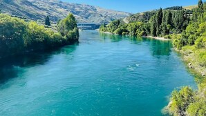 Ein Fluss mit einer Brücke in der Ferne, umgeben von grünen Hügeln und Bäumen.