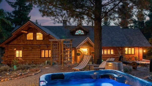 Eine Blockhütte mit Whirlpool, Holzterrasse und einem großen Baum davor.