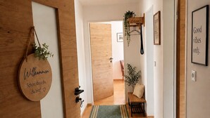 Een hal met een houten deur, een welkomstbord, een groen gekleurd tapijt, een bankje en een ingelijste quote aan de muur.