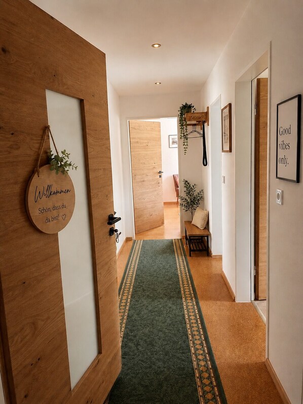 A hallway with a wooden door, a welcome sign, a green patterned carpet, a bench, and a framed quote on the wall. - Vacation apartment with own infrared sauna and terrace - Bavarian Forest (Mauth)