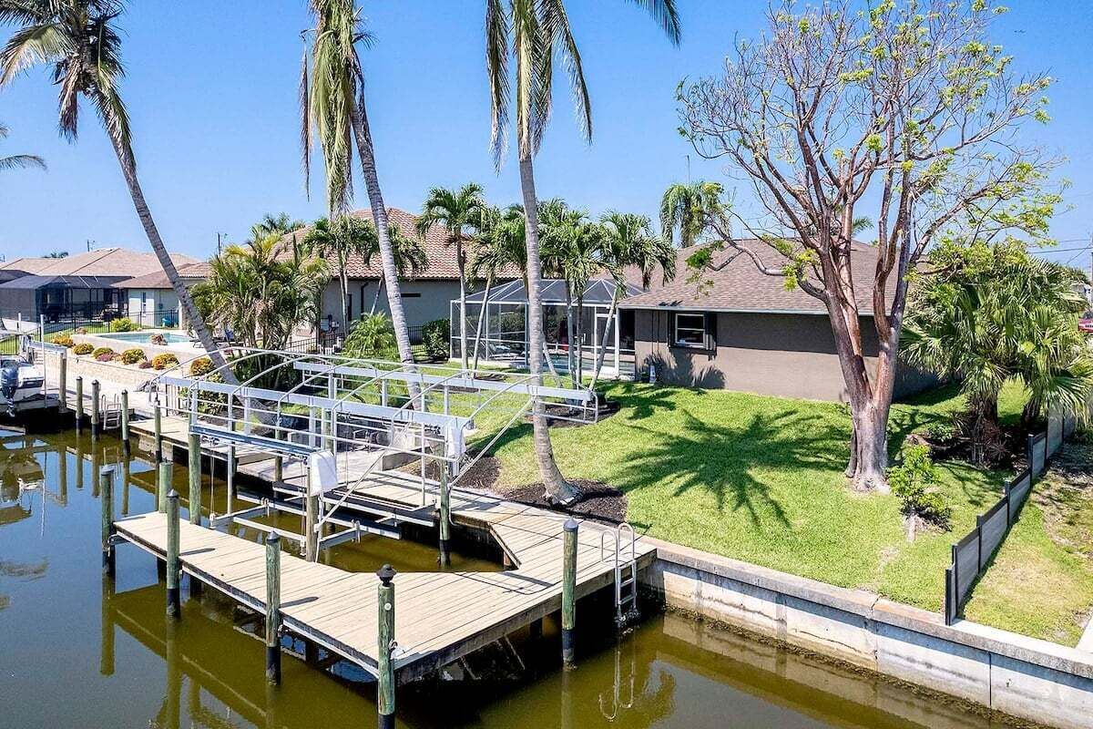 A marina with docks, a swimming pool, and a house with a lawn and palm trees.