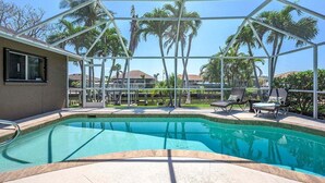 A swimming pool with a glass enclosure, surrounded by lounge chairs and palm trees. - Feeling TipSea | Heated Pool | Gulf Access & Dock (Cape Coral)