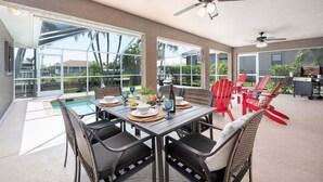 An outdoor dining area with a pool, red chairs, and ceiling fans. - Feeling TipSea | Heated Pool | Gulf Access & Dock (Cape Coral)