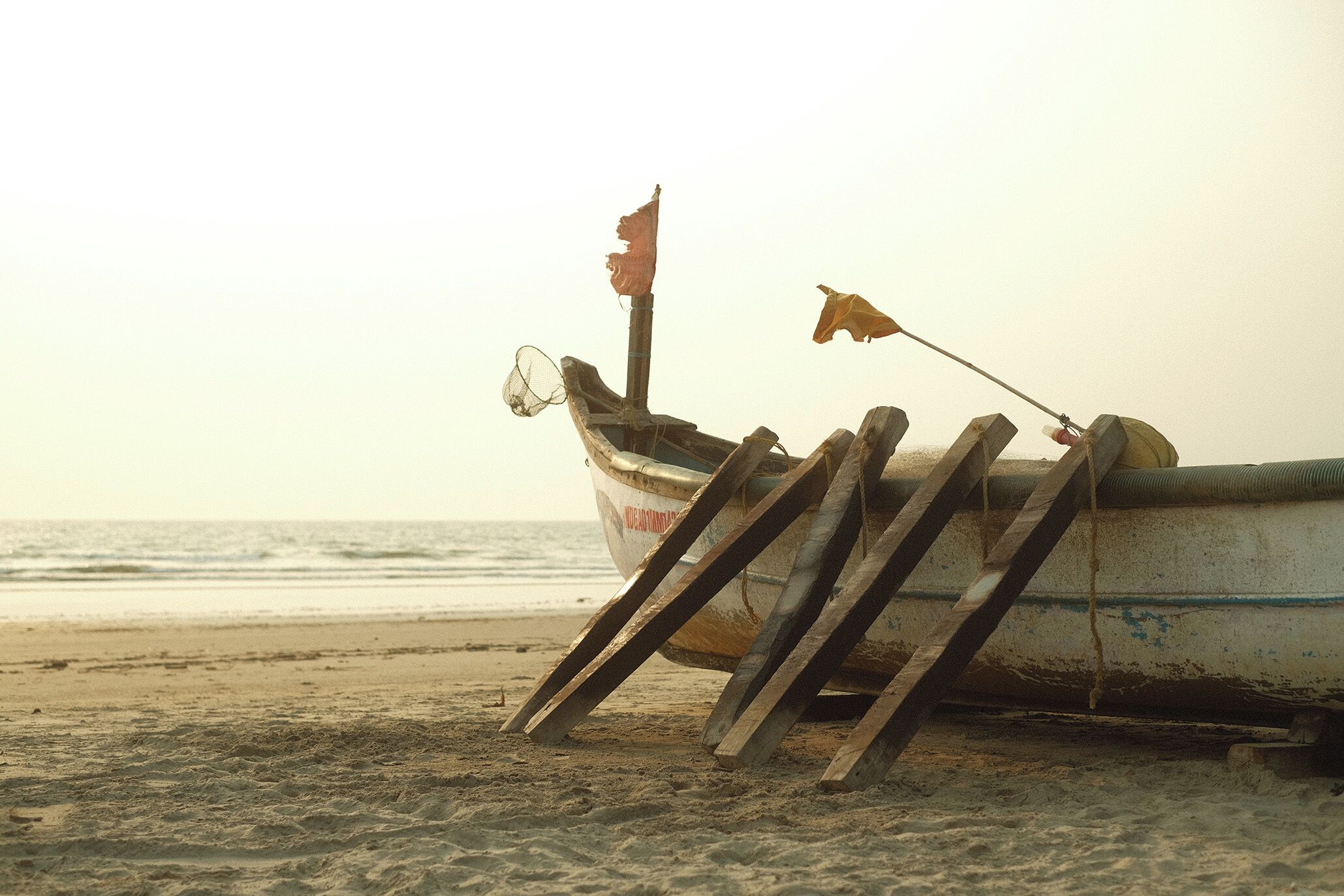 A boat with a flag on a sandy beach near the water.
