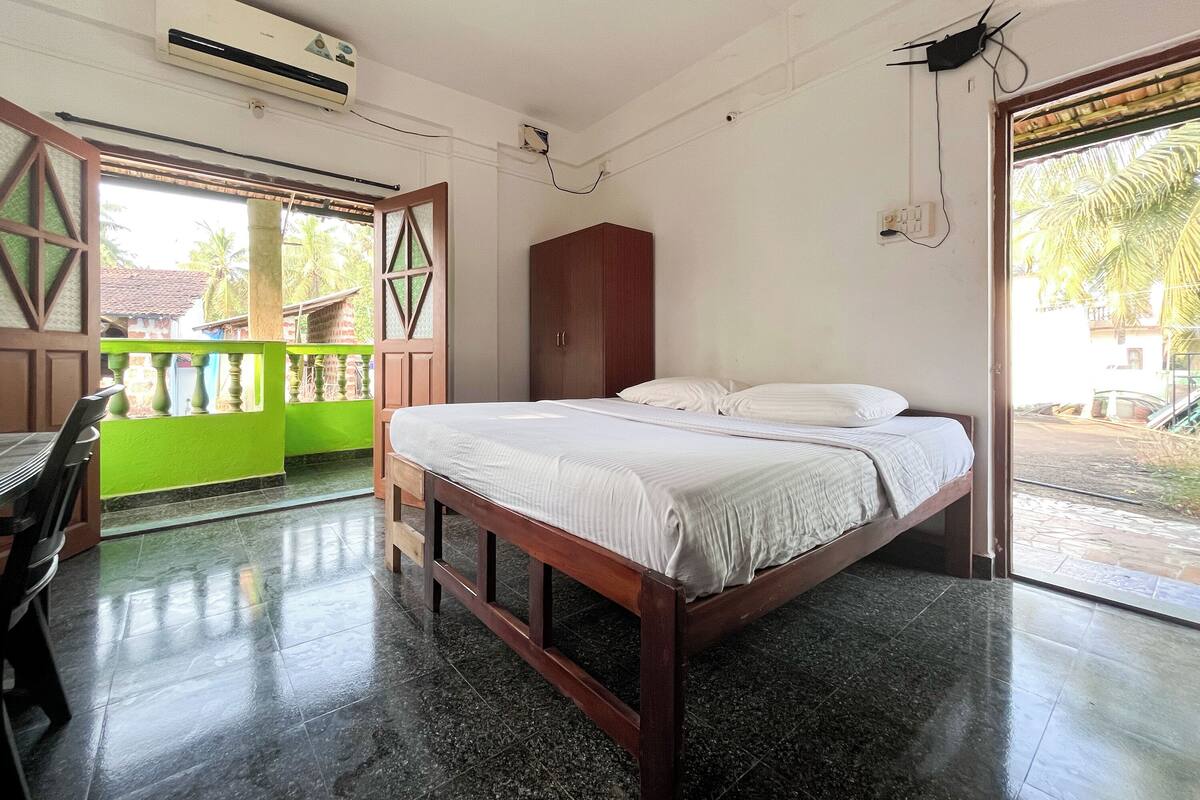 Un dormitorio con cama, armario de madera, pared verde y balcón con vista a palmeras.