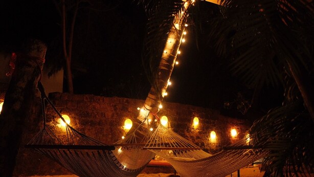 A hammock with string lights hanging above it, set against a stone wall and palm trees. - SPACELAND Mandrem (Mandrem)