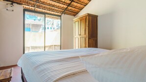 A bedroom with a bed, wooden wardrobe, and a window with a view of buildings. - SPACELAND Mandrem (Mandrem)