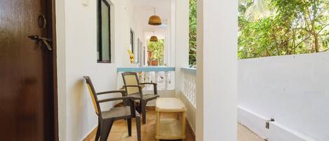 A corridor with chairs and a small table, leading to a balcony with a view of greenery.