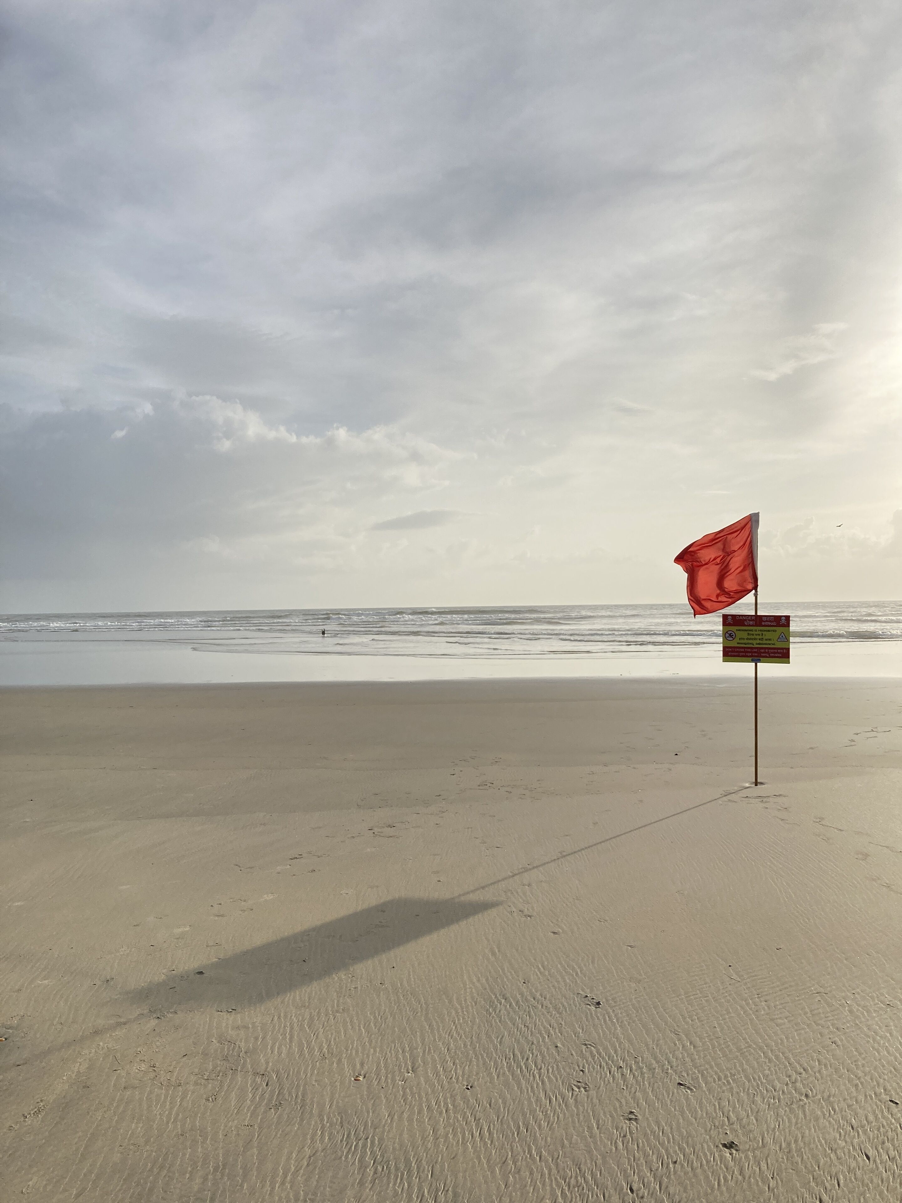 A beach with a red flag and a warning sign.