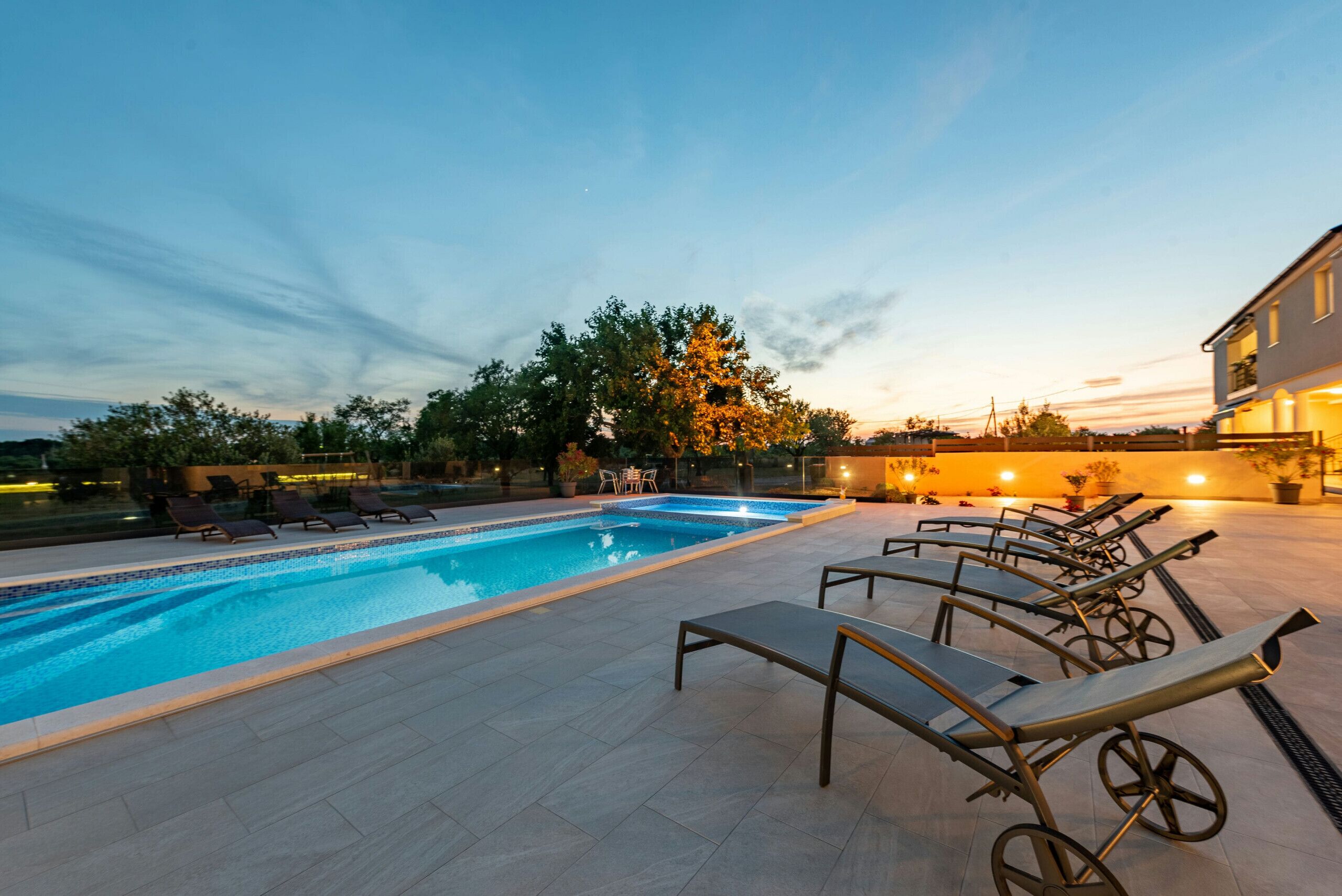 Piscina com espreguiçadeiras e uma árvore ao fundo.