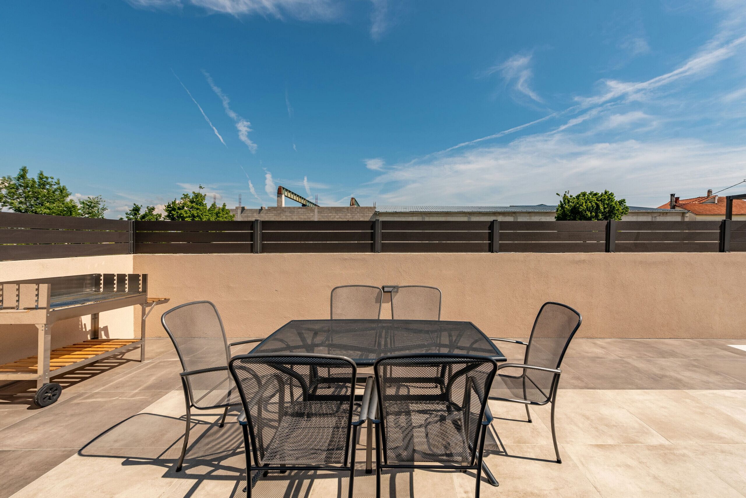 Eine Terrassengruppe im Freien mit Tisch, Stühlen, Grill und Blick auf die Skyline der Stadt.