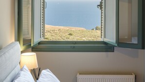 Une chambre avec vue sur la mer, un lit avec du linge de lit blanc, une lampe de chevet et un radiateur.