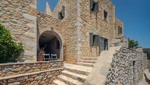 Un bâtiment en pierre avec un escalier raide menant à une porte, un petit porche avec des chaises et un ciel bleu dégagé.