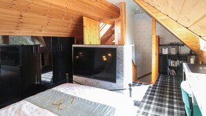 A compact, modern room with wooden walls and a sloped ceiling, featuring a bed, a flat-screen TV, a small kitchenette, and a staircase leading to an upper level. - Swallow Lodge (Morpeth)