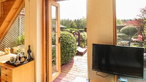 A room with a wooden ceiling, a TV, a wooden cabinet with bottles, and a view of a garden through an open door. - Swallow Lodge (Morpeth)