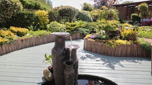 A garden with a stone fountain, wooden deck, and various plants. - Swallow Lodge (Morpeth)