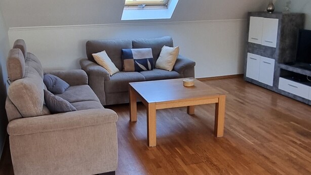 Una sala de estar tipo loft con techo inclinado, tragaluz, sofá, mesa de centro y mueble para televisor.