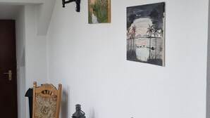 Un comedor con una mesa y sillas de madera, una lámpara de pared y dos cuadros.