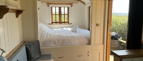 Um quarto aconchegante com uma cama, uma escrivaninha com um laptop e uma janela com vista para o verde.