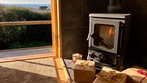 A cozy room with a wood-burning stove, a large window overlooking a scenic view, and several wrapped gifts on the floor.