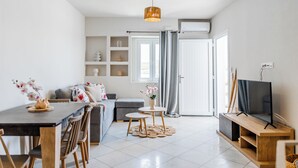 Una sala de estar moderna con comedor, un sofá gris, un televisor y un ventanal con cortinas.