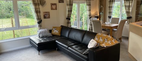 A cozy living room with a black leather sectional sofa, a dining table with chairs, and large windows with curtains.