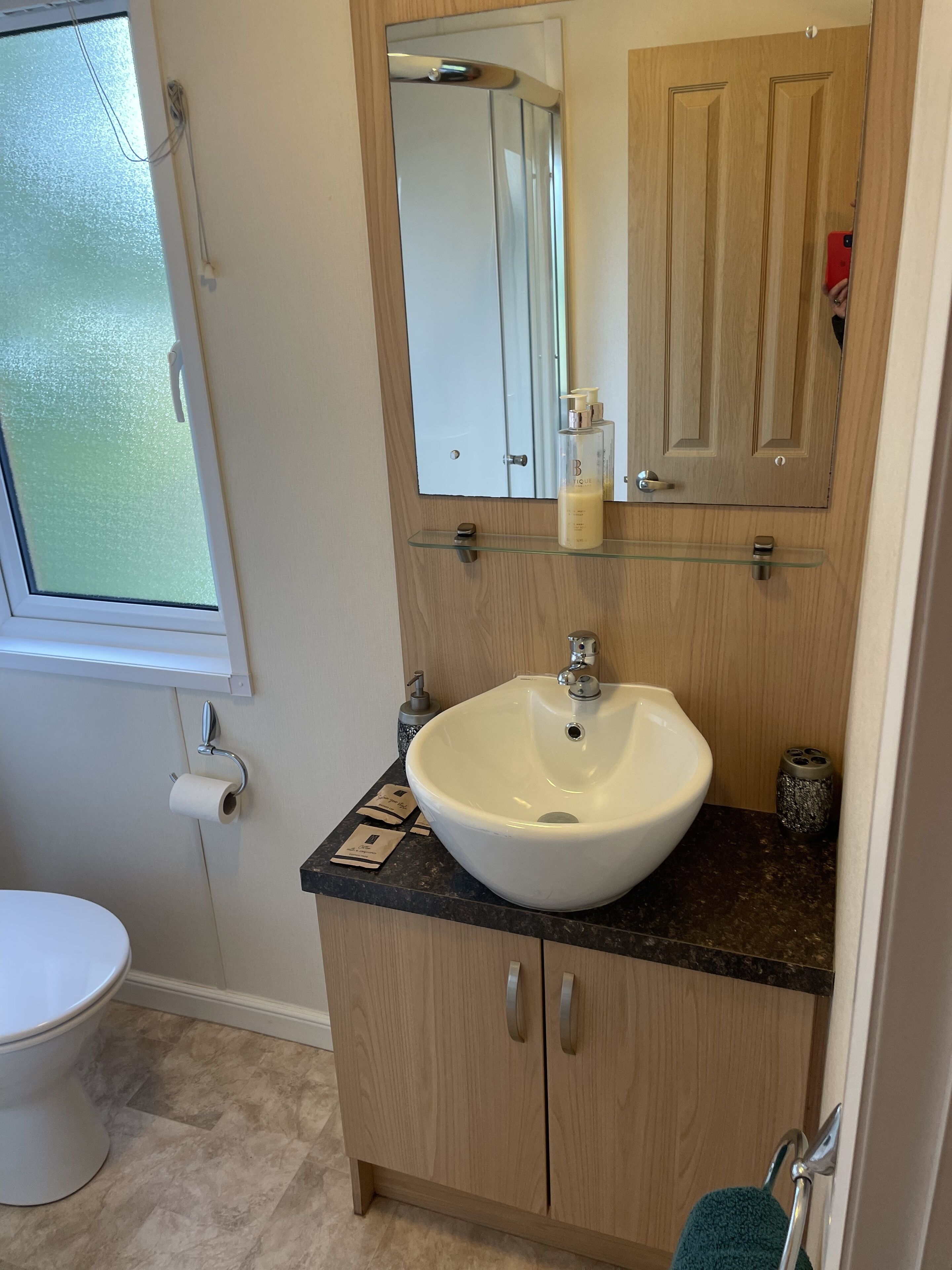 Un bagno con un lavandino bianco, uno specchio sopra, un water e una finestra.