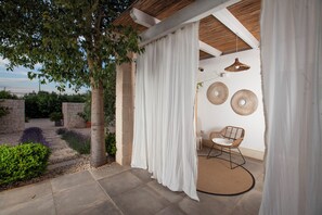 A covered outdoor seating area with a wicker chair and woven wall decor. - Casa Mia in Puglia (Conversano)