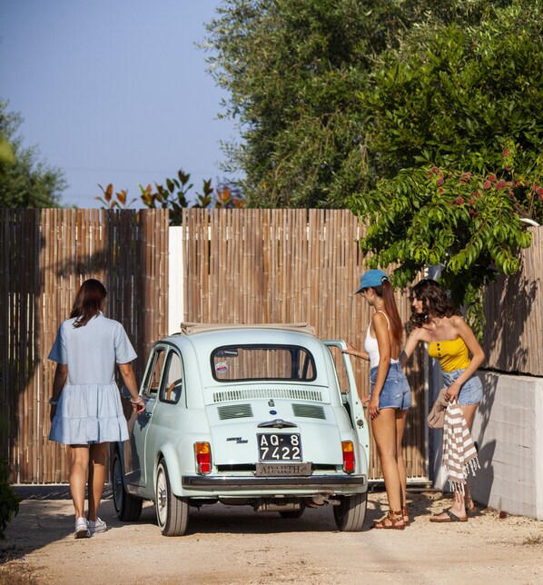 A vintage car parked in front of a wooden fence with a group of people standing nearby.