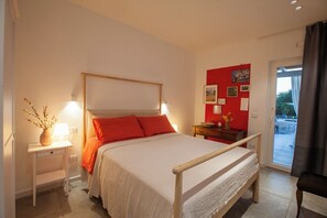 A bedroom with a bed, bedside tables, a nightstand, a red wall with pictures, and a view through a glass door. - Casa Mia in Puglia (Conversano)