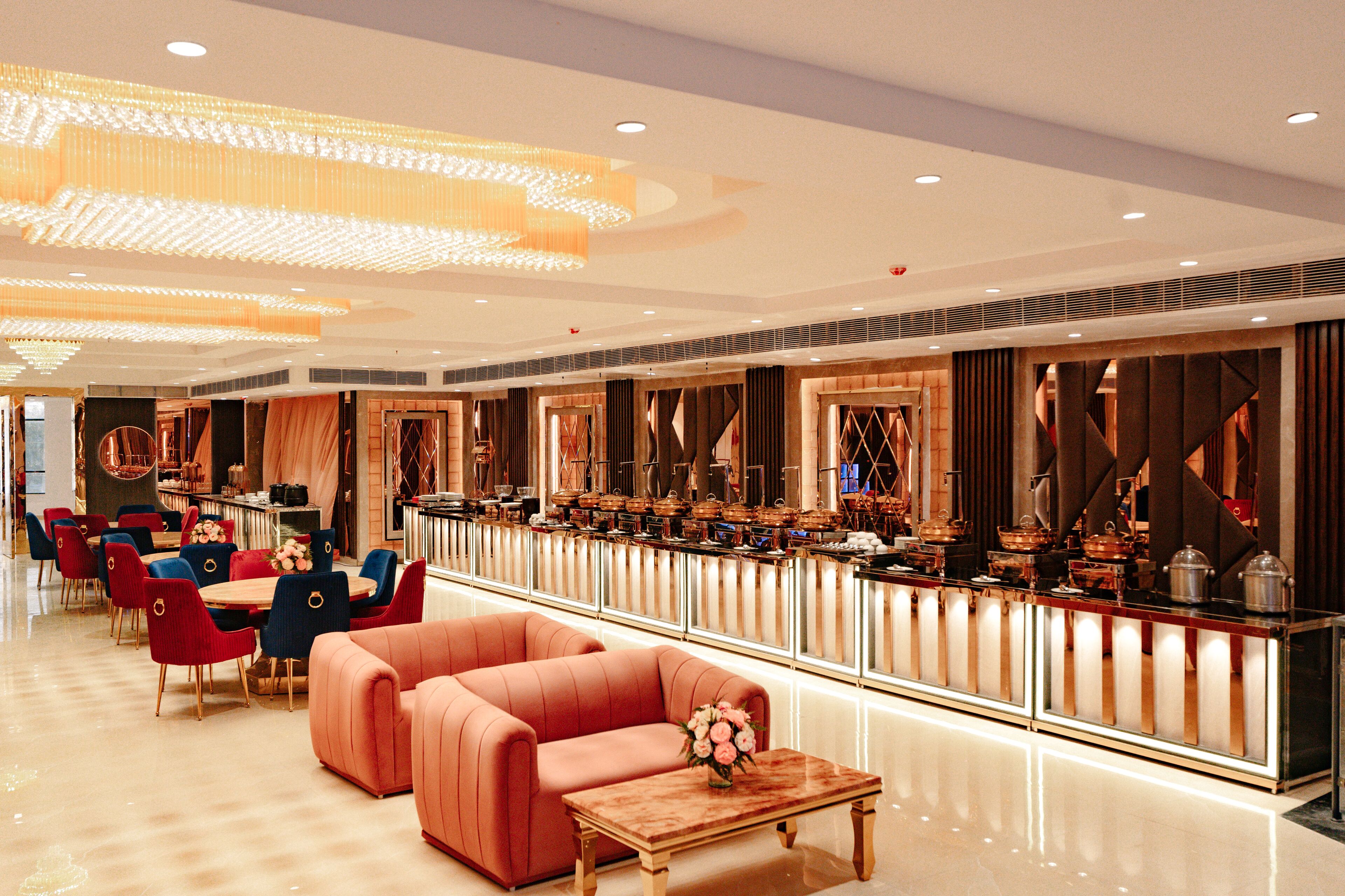 A spacious hotel lobby with a long reception desk, multiple seating areas, and a modern chandelier.