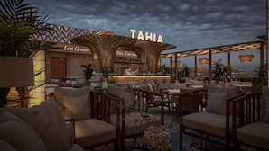 Un bar en la azotea con letrero 'TAHIA', mesas al aire libre y vistas de la ciudad.