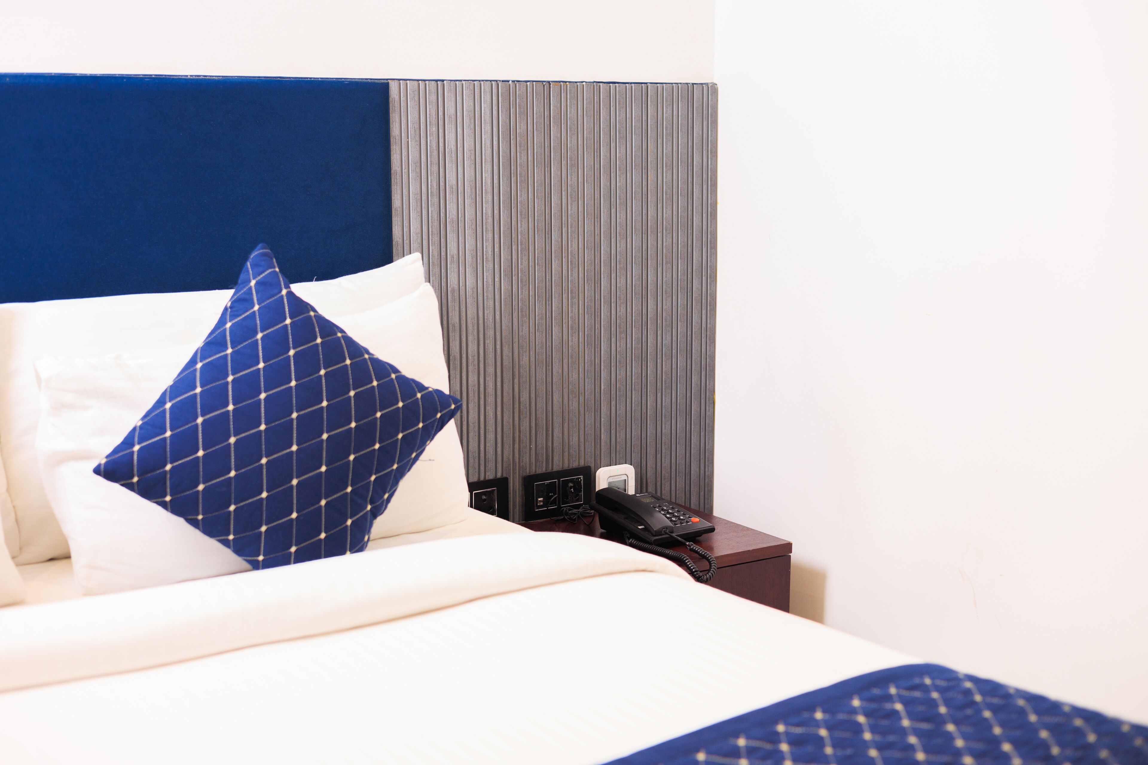 A hotel room with a bed, a nightstand, a telephone, and a wall panel.