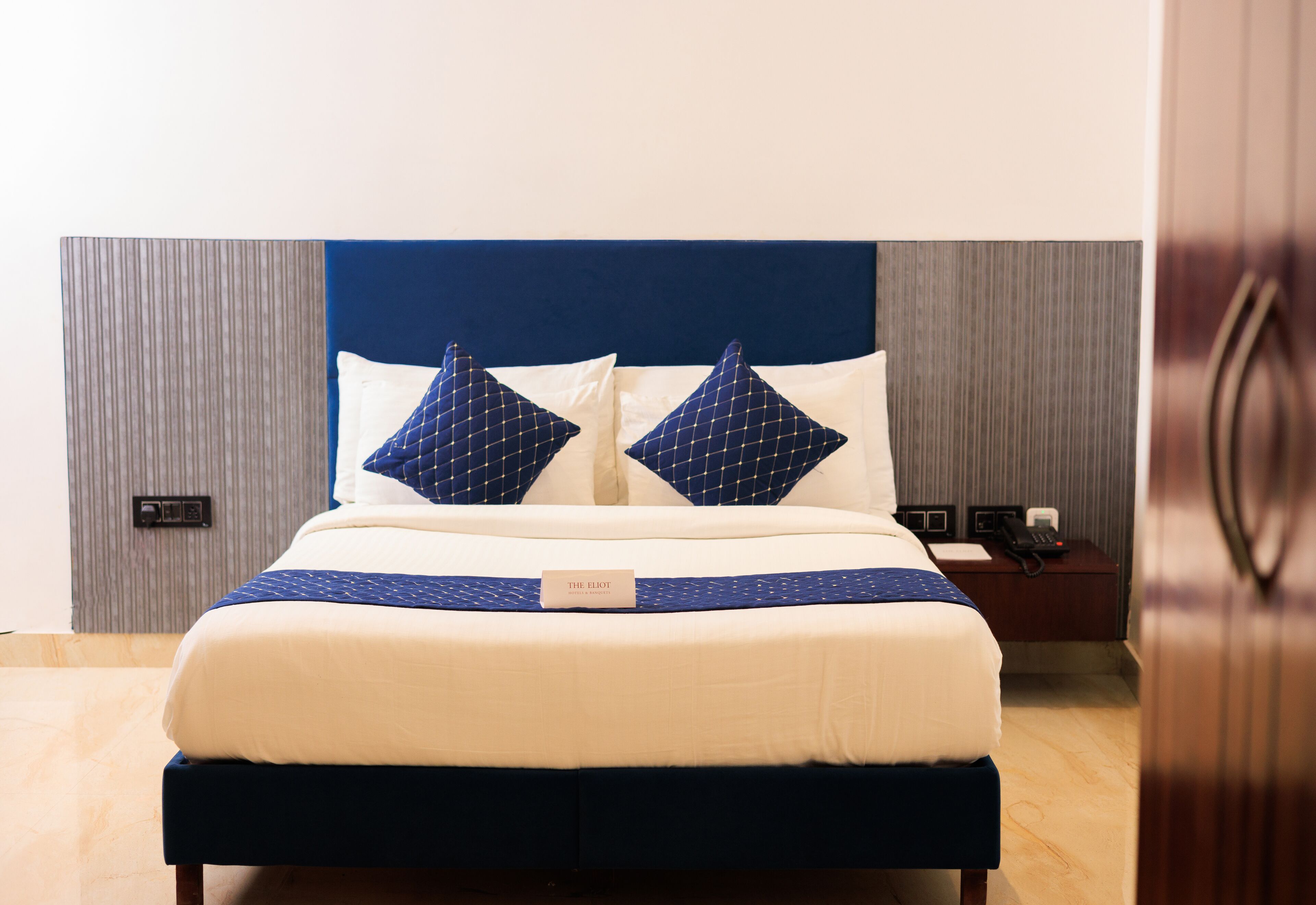 Una cama bien hecha con un cabecero azul, ropa de cama blanca y dos almohadas decorativas.