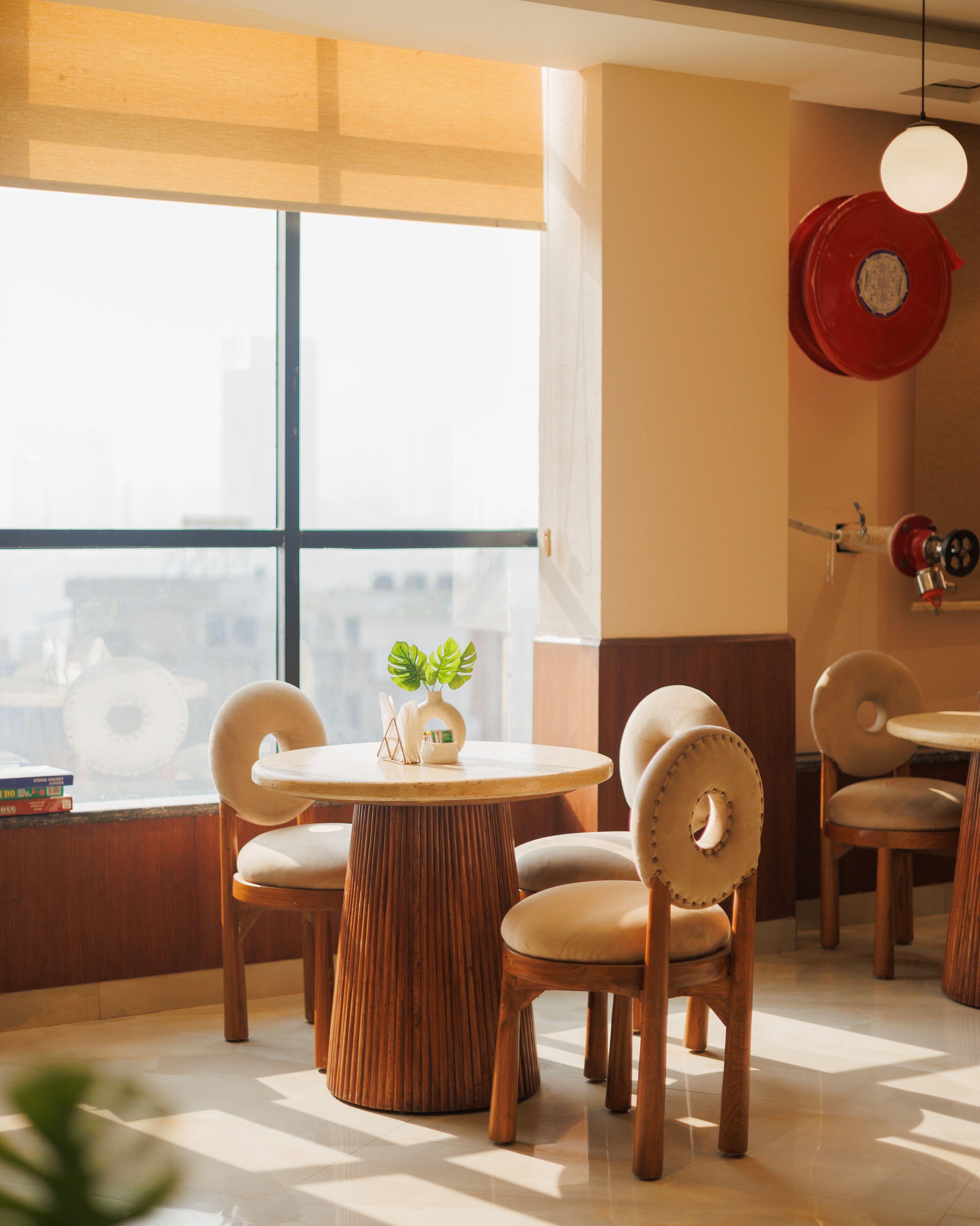 A modern interior with a round wooden table, cushioned chairs, and a large window.