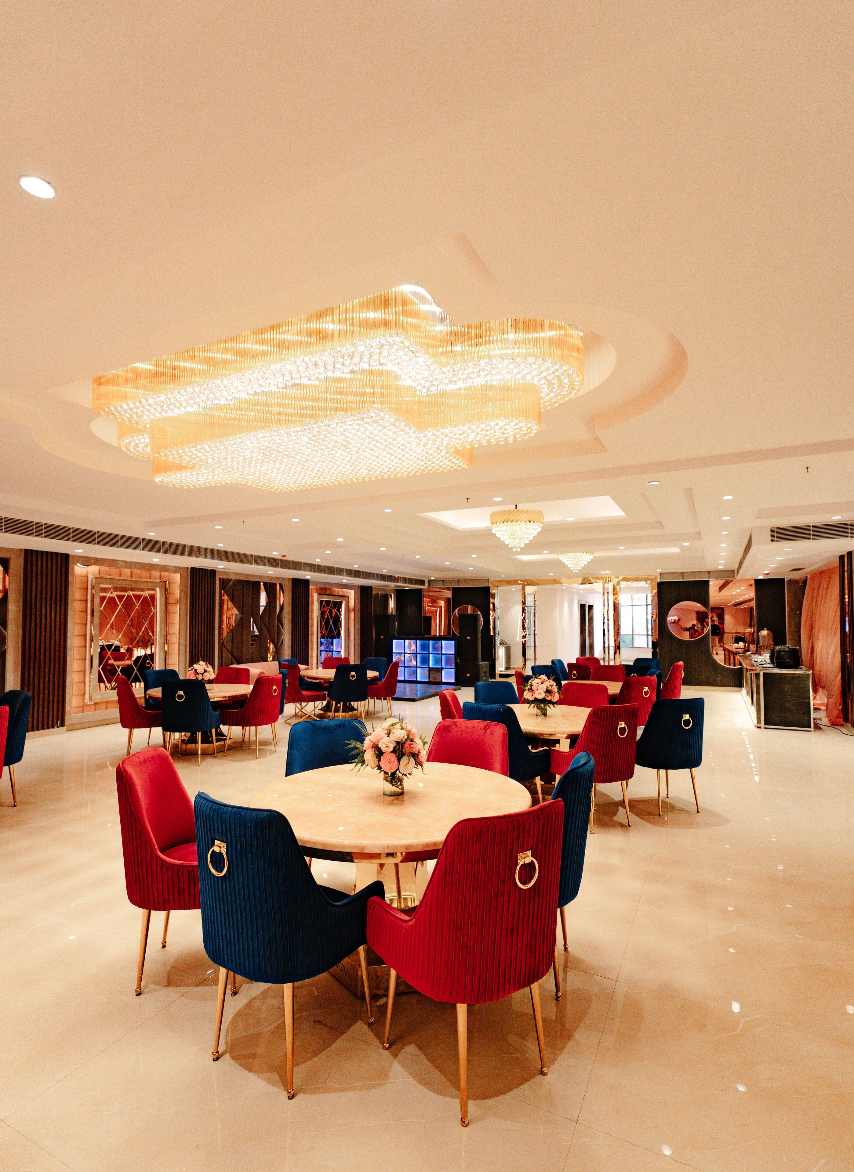 A spacious dining area with round tables and chairs, a large chandelier, and a modern interior design.
