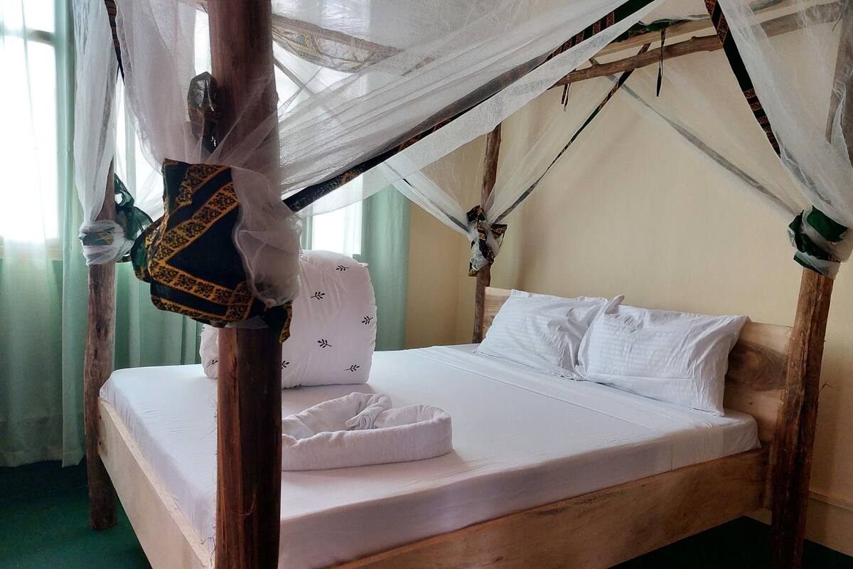 Una cama con estructura de madera, ropa de cama blanca y dosel.
