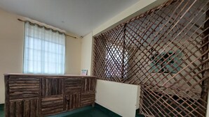 Ein Empfangsbereich mit einem Holzbüro, einem Fenster mit durchsichtigen Vorhängen und einer dekorativen Gitterwand.