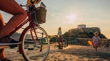 En strandscene med en cykel, en person i leopardmønstrede sko, og et barn med et strandlegetøj.